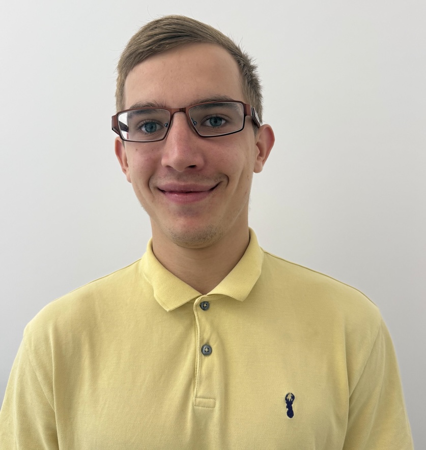 Młody mężczyzna w okularach, z krótkimi włosami, uśmiecha się